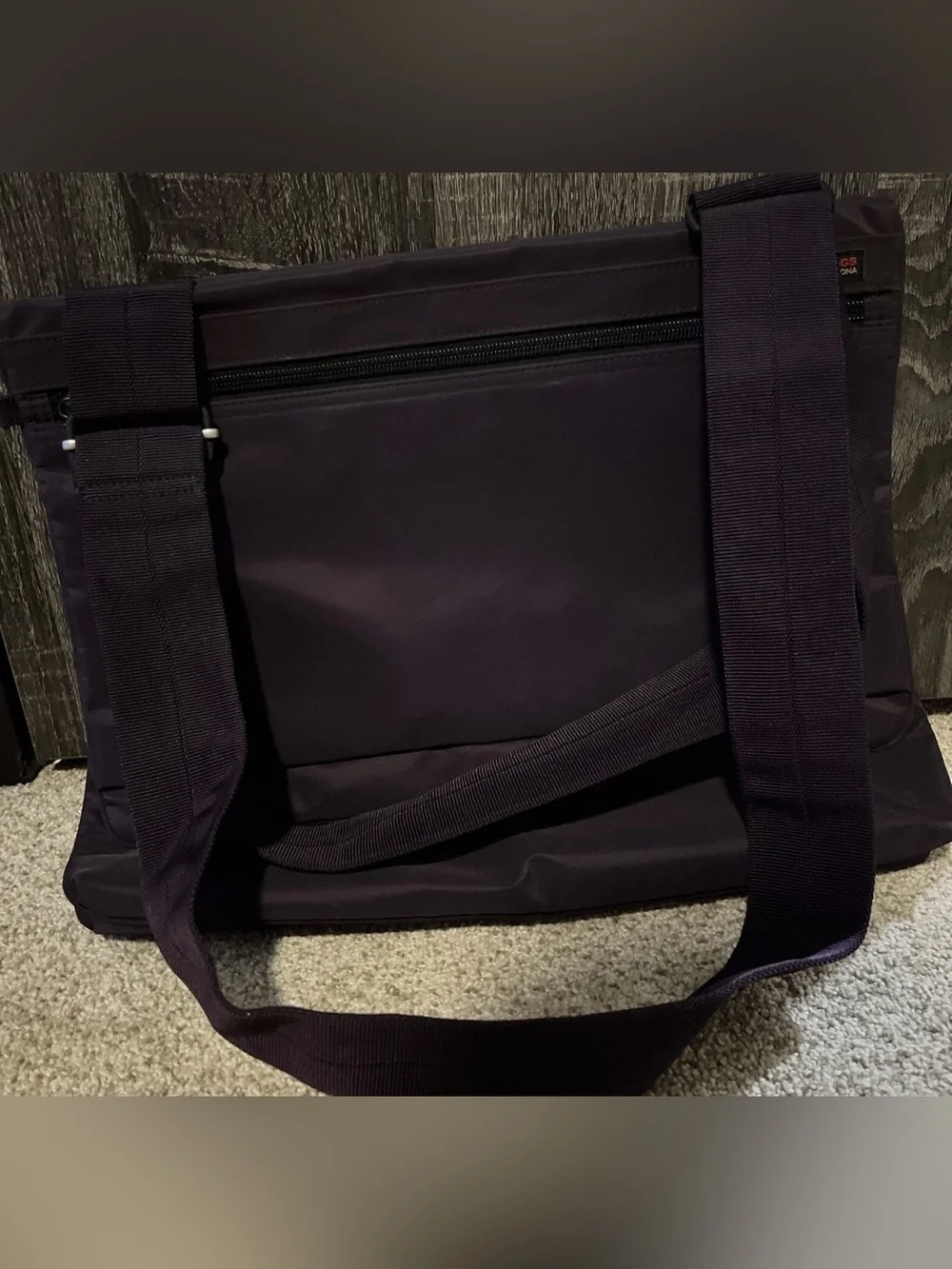 This grey Hedgren crossbody bag features a distinctive red label showcasing the